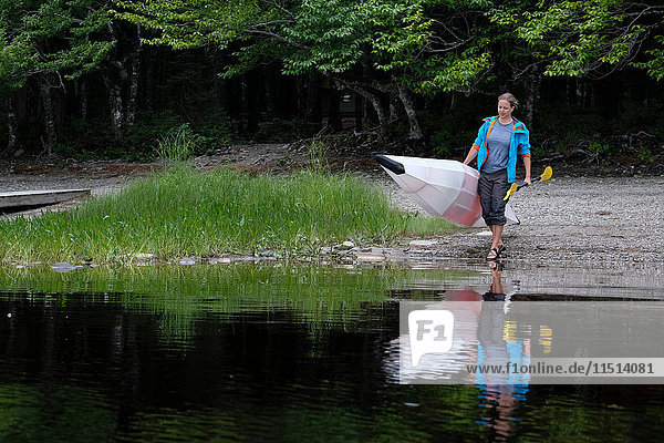 Kayaker carrying kayak to water edge  Kejimkujik Lake  Nova Scotia  Canada
