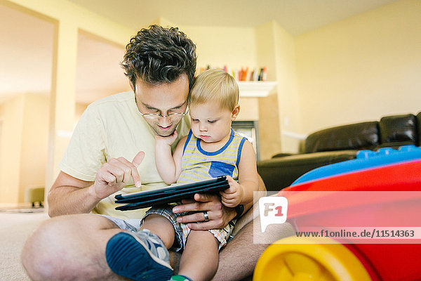 Vater und kleiner Sohn spielen zu Hause zusammen und schauen sich ein digitales Tablet an