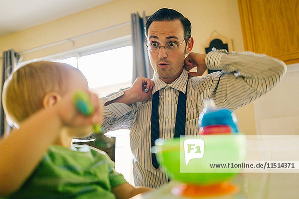 Vater und kleiner Sohn in der Küche  Vater legt Krawatte an  während der Sohn frühstückt