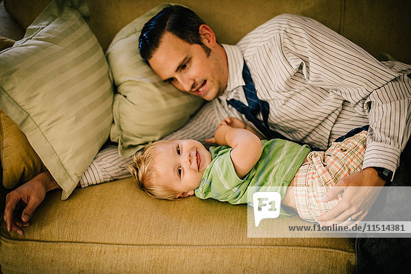 Vater und kleiner Sohn liegen zusammen auf dem Sofa