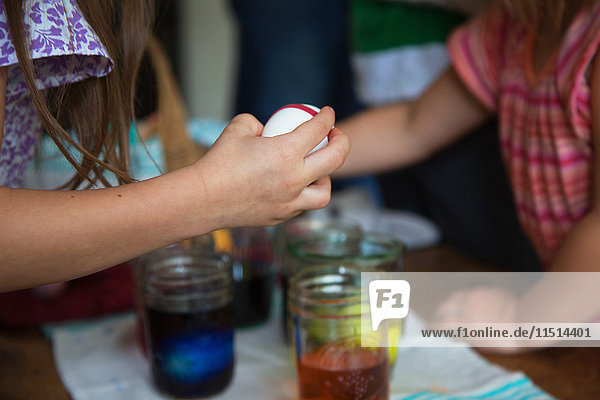 Hände von zwei jungen Schwestern  die sich bei Tisch darauf vorbereiten  Ostereier in Gläsern zu färben