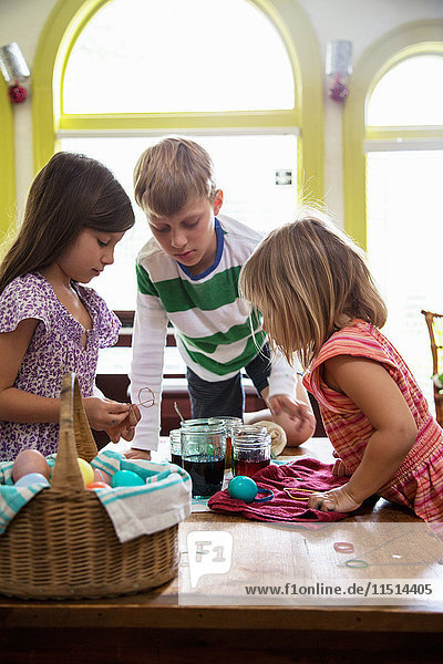 Junge und zwei Schwestern beobachten beim Färben von Ostereiern bei Tisch