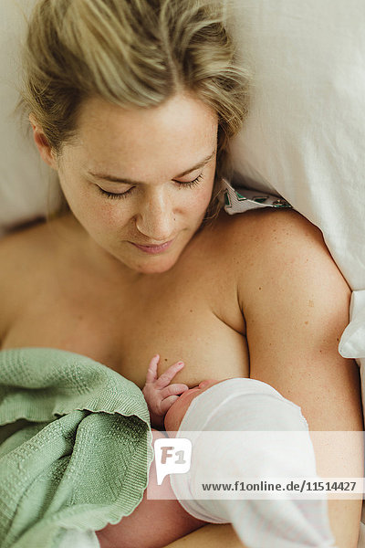 Draufsicht einer mittleren erwachsenen Frau  die eine neugeborene Tochter im Bett stillt