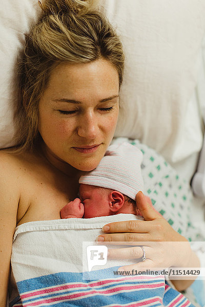 Draufsicht einer mittelgroßen erwachsenen Frau  die im Bett liegt und ihre neugeborene Tochter wiegt