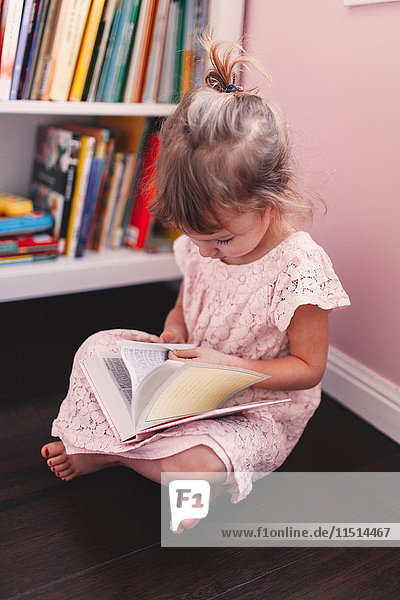 Girl sitting on playroom floor reading book