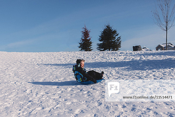 Junge mit Strickmütze rodelt schneebedeckten Hügel hinunter