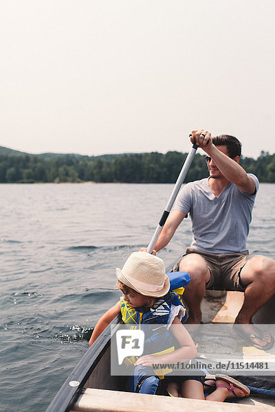 Young man and daughter rowing across lake in rowing boat