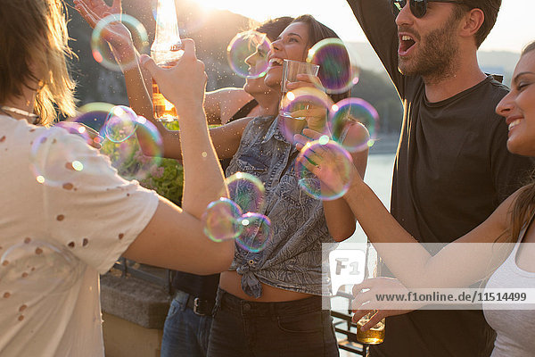 Erwachsene Freunde spielen mit schwebenden Blasen auf Dachterrassenparty