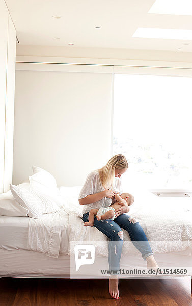 Mid adult woman sitting on bed breastfeeding baby son