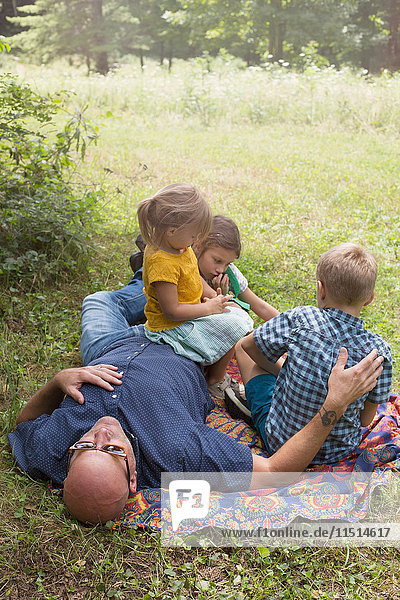 Vater und Kinder entspannen sich auf einer Decke im Gras
