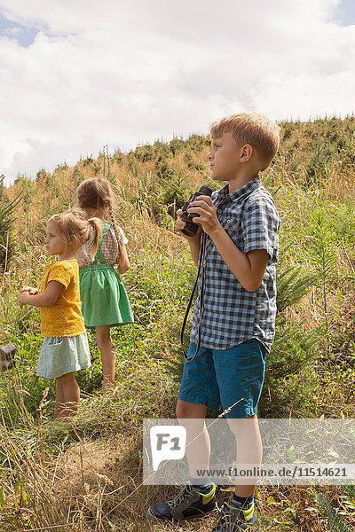 Three young children exploring  outdoors  boy using binoculars