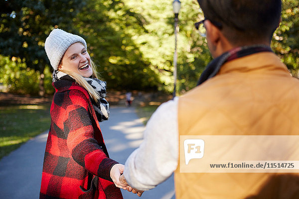 Junge Frau führt ihren Freund im Park an der Hand