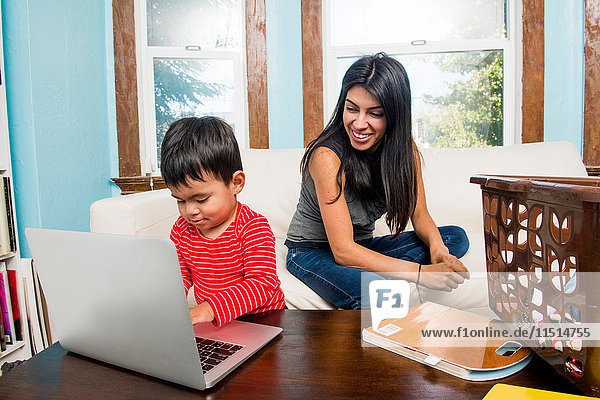 Männliches Kleinkind mit Mutter  die zu Hause am Laptop tippt