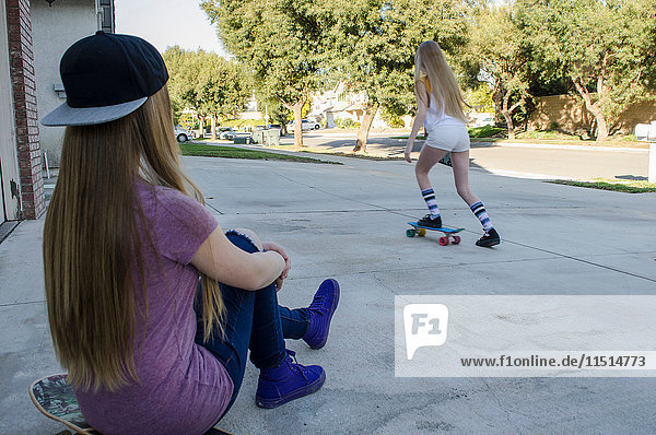 Teenagerin beobachtet Schwester beim Skateboarden auf dem Bürgersteig