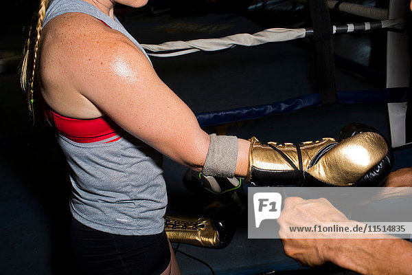 Trainer tying boxing glove laces for female boxer in gym