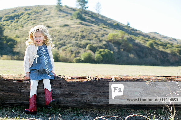 Porträt eines auf einem Baumstamm sitzenden Mädchens in roten Cowboy-Stiefeln