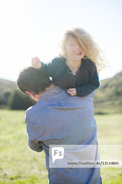 Portrait of girl being carried over father's shoulder in field