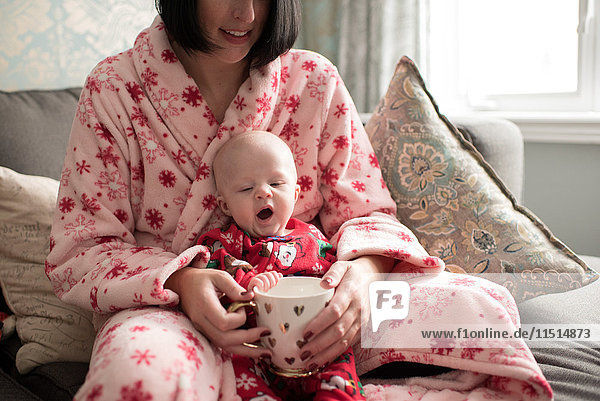 Mother and baby boy holding mug  sitting on sofa