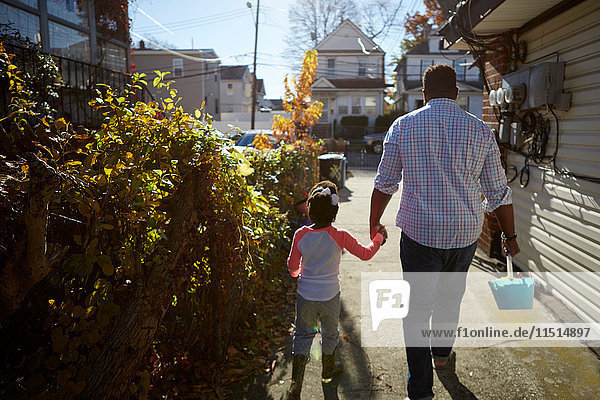 Father and daughter holding hands walking with bucket