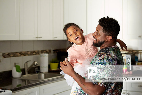 Father carrying daughter in kitchen