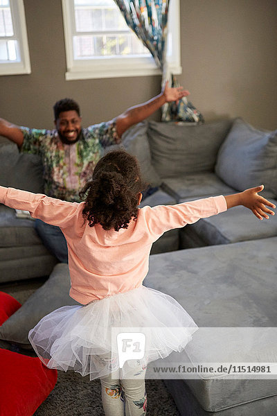 Girl in tutu and father on sofa with open arms