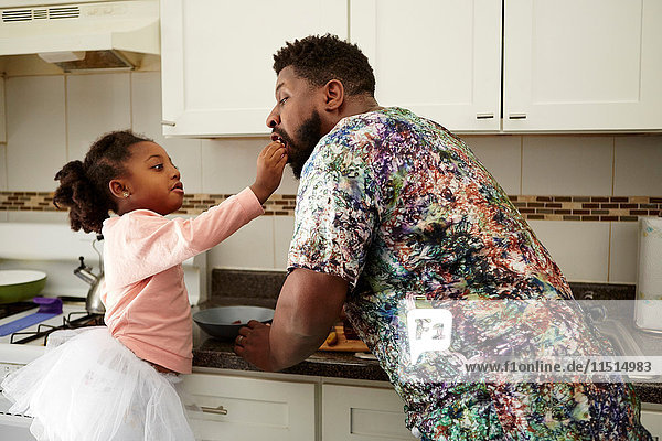 Girl feeding father in kitchen