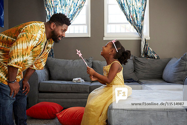 Mann spielt mit Tochter im Feenkostüm im Wohnzimmer