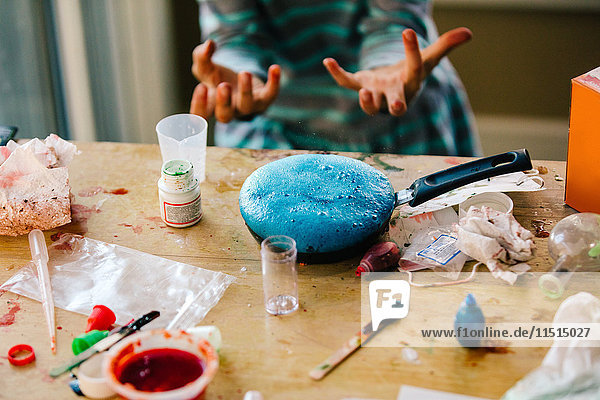 Hände eines Mädchens beim wissenschaftlichen Experiment  blaue Flüssigkeit schäumt in der Bratpfanne