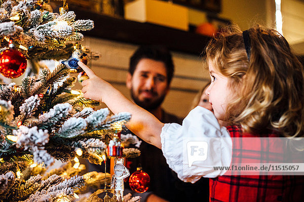 Weibliches Kleinkind mit Eltern  die auf eine Christbaumkugel zeigen