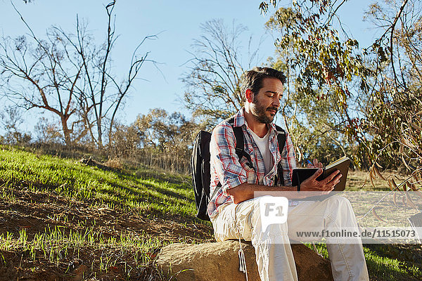 Mittelgroßer erwachsener Mann wandert,  sitzt auf einem Felsblock und liest Buch