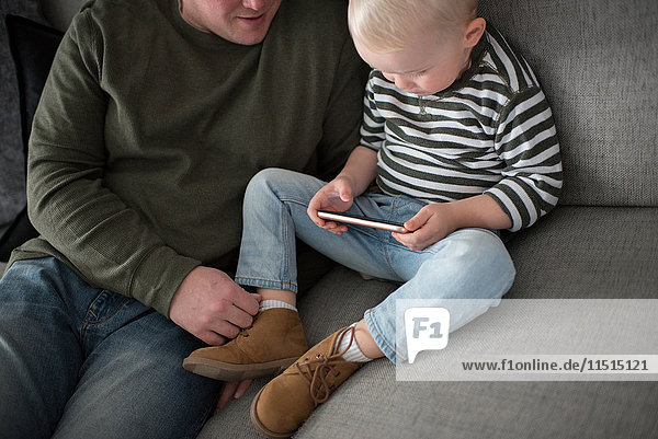 Vater und Sohn sitzen auf dem Sofa  der Sohn schaut auf das Smartphone