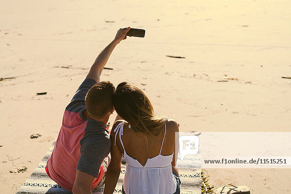 Rear view of couple sitting on beach taking smartphone selfie  Newport Beach  California  USA