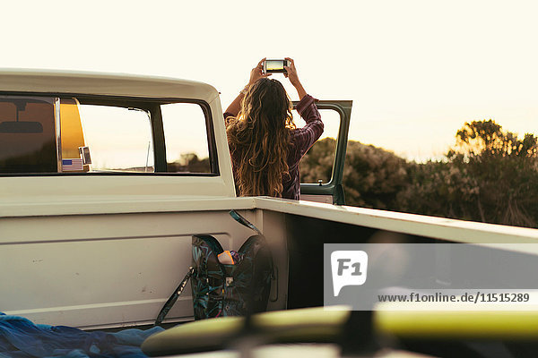 Rear view of young woman with pickup truck photographing coast at Newport Beach  California  USA