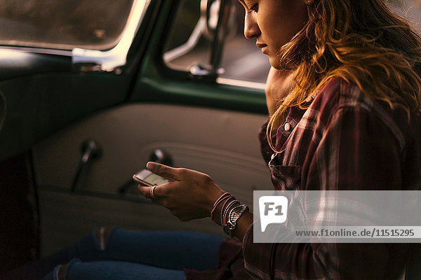 Young woman looking at smartphone in front seat of pickup truck at Newport Beach  California  USA
