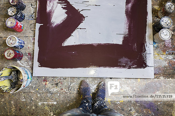 Legs of Mari man standing near paint cans and canvas on floor