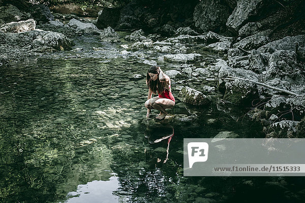 Kaukasische Frau hockt auf Felsen an einem Wasserbecken