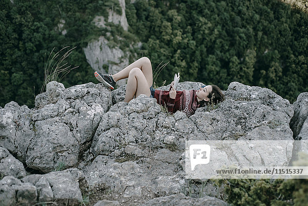 Kaukasische Frau liegt auf einem Bergfelsen und liest eine Zeitschrift