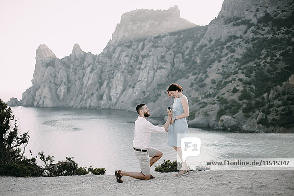 Kaukasischer Mann macht einer Frau am Strand einen Heiratsantrag