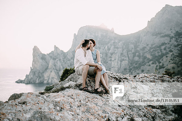 Kaukasisches Paar sitzt auf Felsen am See