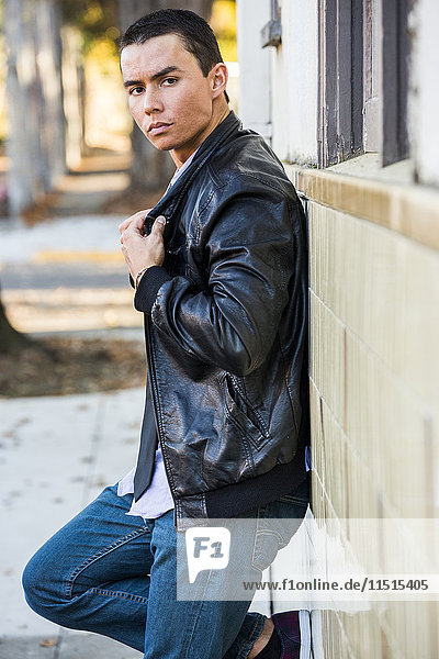 Serious Mixed Race man leaning on wall wearing leather jacket