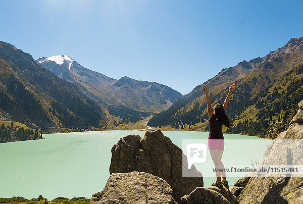 Caucasian woman celebrating on rocks near mountain lake