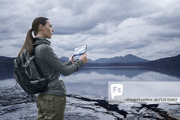 Caucasian woman photographing mountain lake with digital tablet