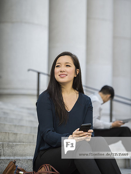 Chinese businesswoman sitting on staircase holding cell phone