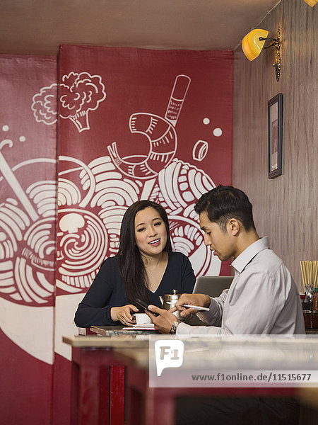 Chinesische Geschäftsleute  die im Restaurant mit ihrem Handy telefonieren
