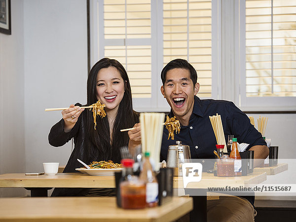 Smiling Chinese couple holding noodles with chopsticks in restaurant