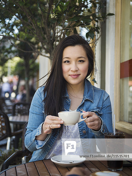 Smiling Chinese woman drinking coffee at outdoor cafe