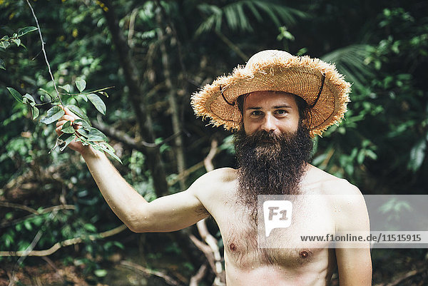 Kaukasischer Mann mit nackter Brust hält Ast im Wald