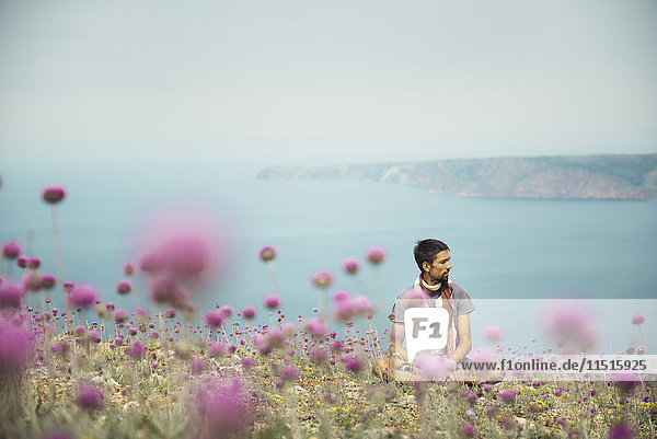 Kaukasischer Mann sitzt in einem Blumenfeld in der Nähe des Ozeans