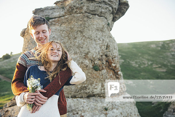 Kaukasisches Paar umarmt in der Nähe von Felsen mit Blumenstrauß