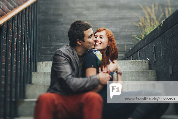 Kaukasisches Paar sitzt auf einer Treppe und küsst sich